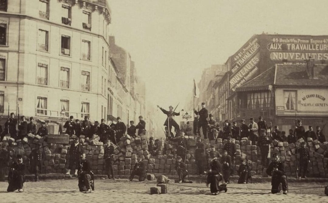 Fotografia de uma barricada de pedras numa rua de Paris, com homens armados e moradores posando.