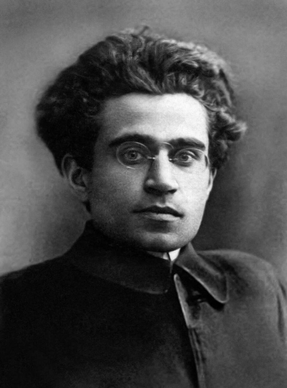 Retrato em preto e branco de Antonio Gramsci jovem, de óculos e cabelos volumosos.
