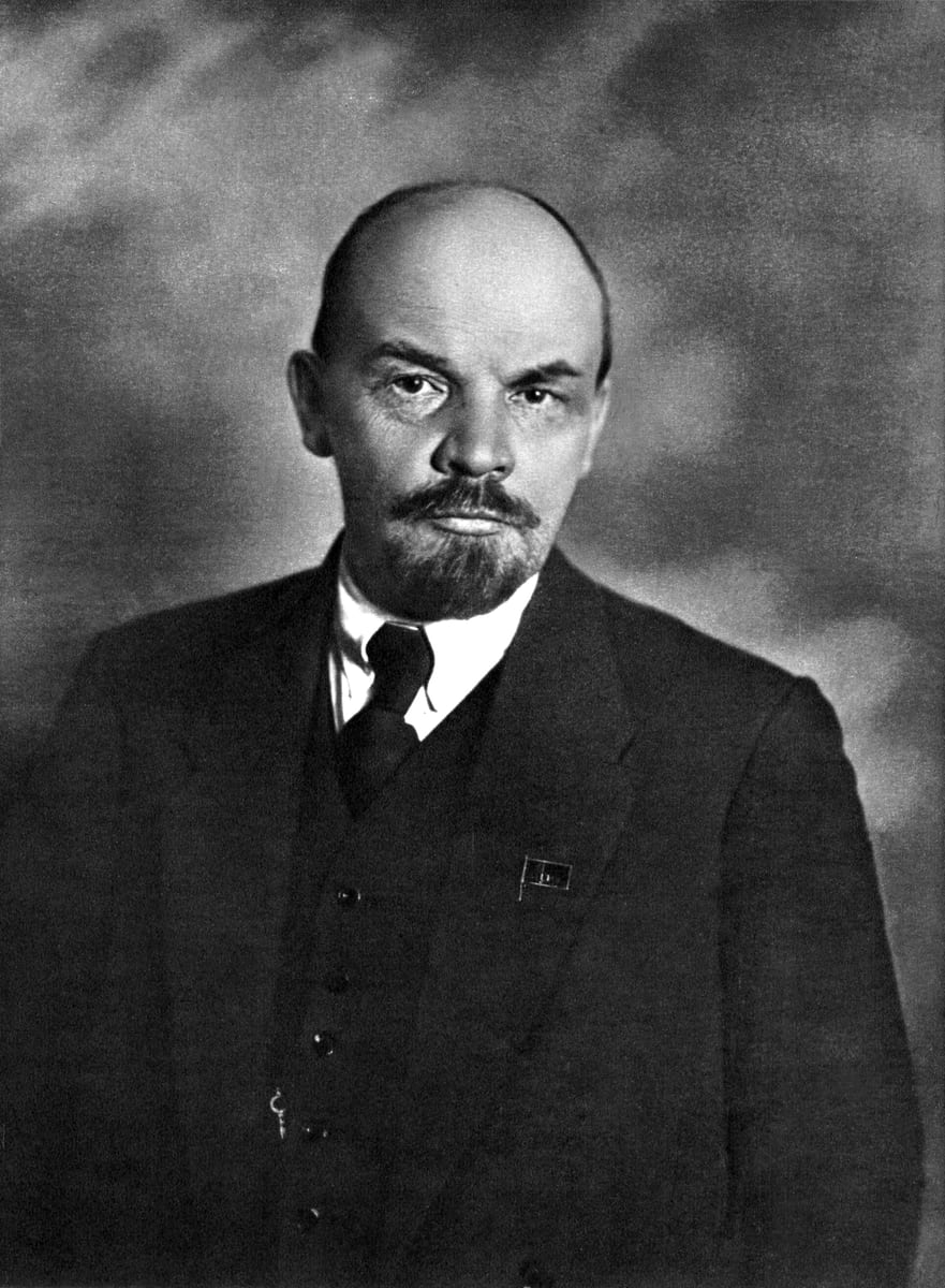 Fotografia em preto e branco de Lenin de pé, de terno e colete, com o polegar no bolso do colete.